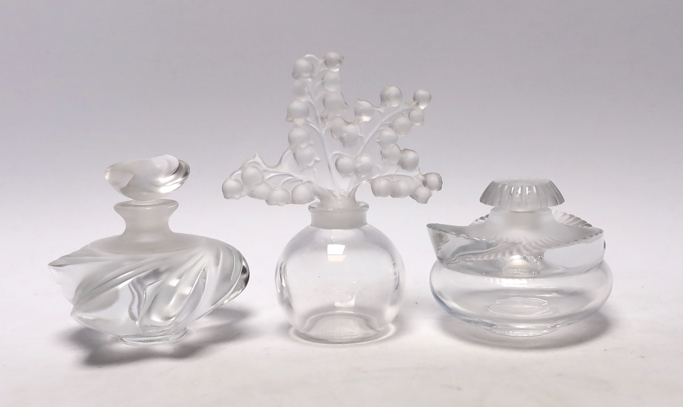 Three Lalique glass scent bottles and stoppers, one with Lily of the Valley stopper, 12cm